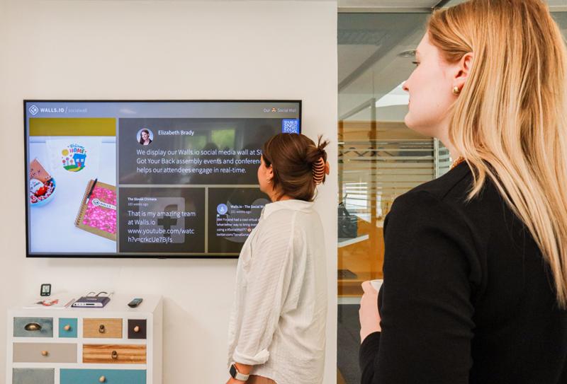 Deux personnes regardent un écran d'information au mur d'un bureau